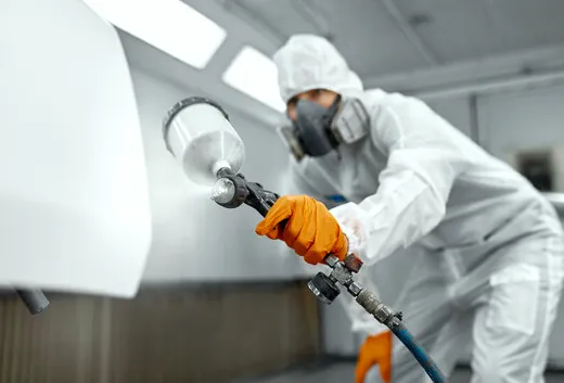 Painter in protective gear spray-coating steel doors